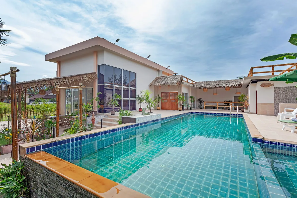 A villa pool and thatched terrace photographed in daylight.